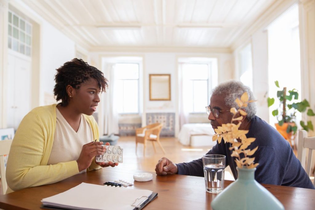 Young caregiver meeting with an elderly man at his dining table during a home care visit