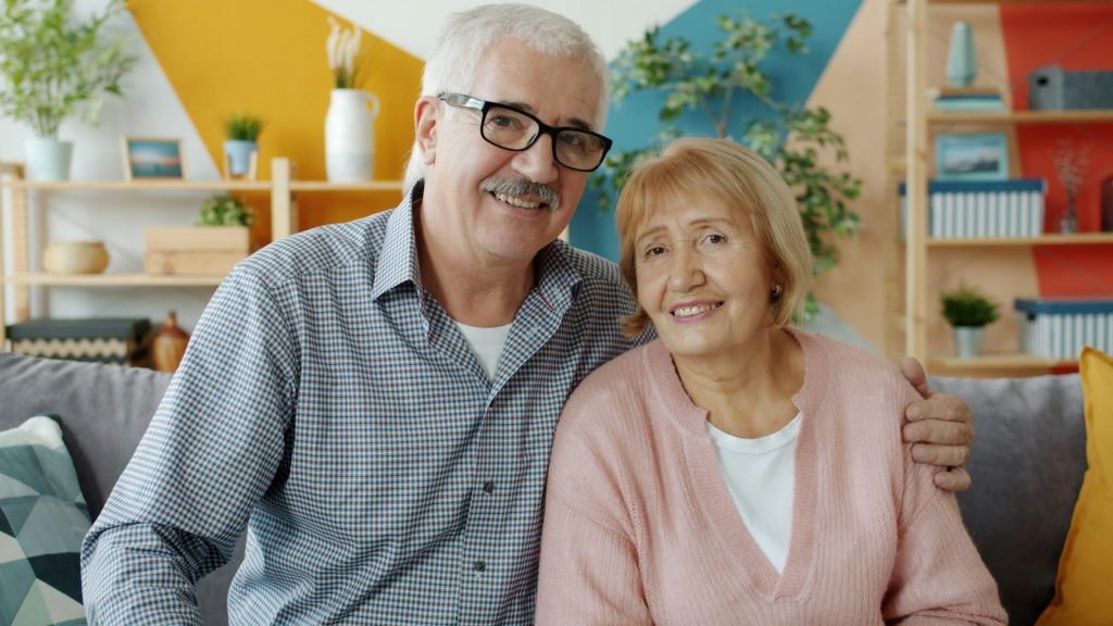 an older husband and wife sitting together on a bench, holding hands (caring for a spouse with dementia)