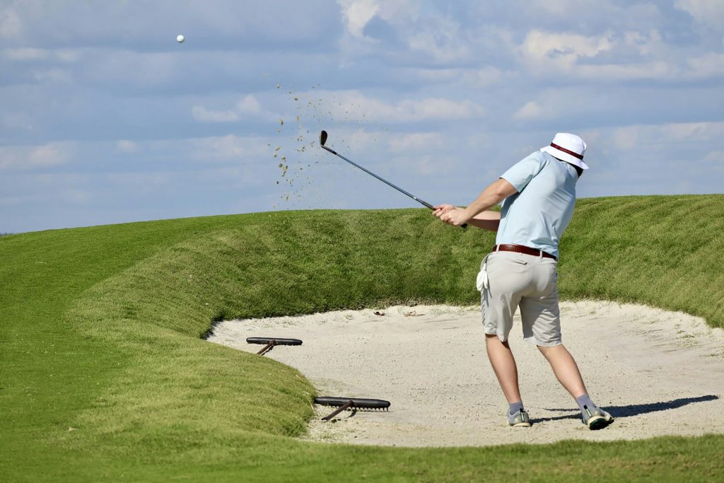 An older golfer in a white cap playing out of a bunker, the kind of outing dementia care in Palm Beach Gardens can keep going